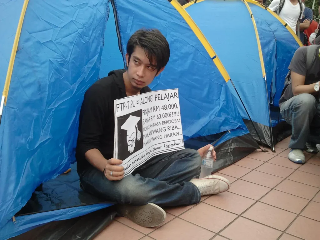 Adam Adli (Ketua AMK) memegang sepanduk bantah PTPTN. Kini timbalan Menteri Belia dan Sukan, dahulunya merupakan aktivis popular dalam menggerakkan kempen bantah PTPTN pada tahun 2012. Setelah berada dalam kerajaan, beliau menjadi alat reformis PKR. Hujah beliau bahawa "mansuh PTPTN sukar untuk dilaksanakan disebabkan faktor ekonomi".